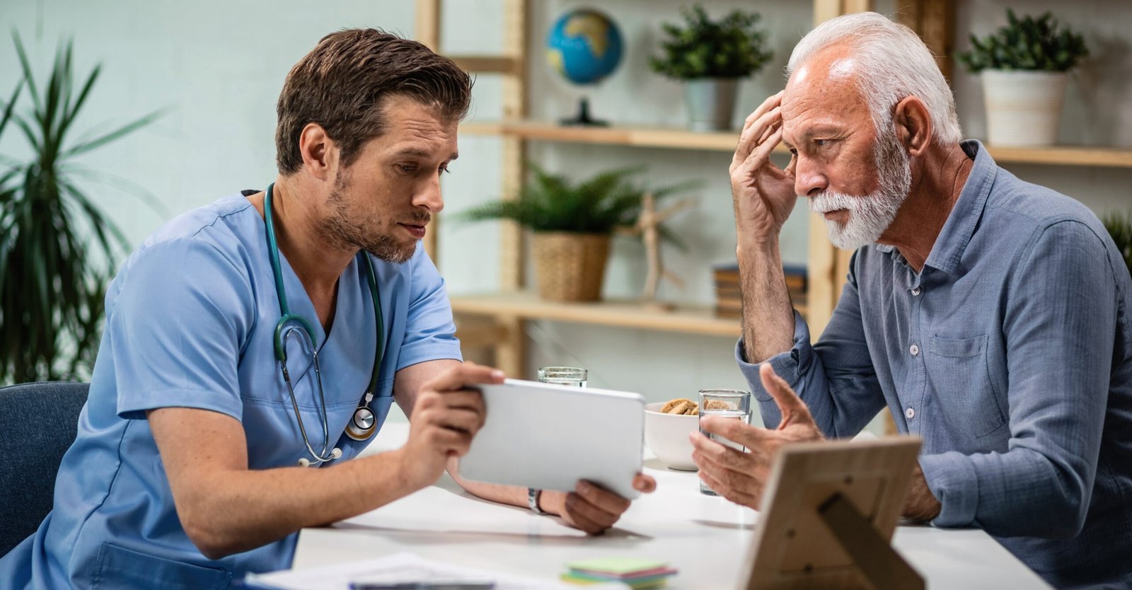 Worried senior patient and his doctor using touchpad during medical appointment.