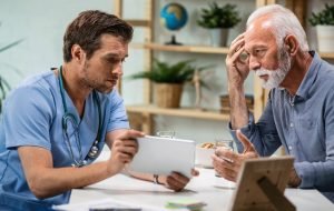Worried senior patient and his doctor using touchpad during medical appointment.